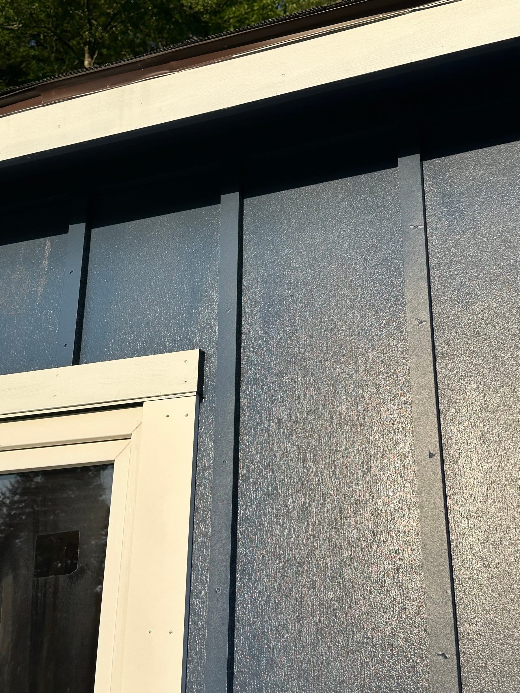 Close detail of dark navy board-and-batten siding beside a cream-trimmed window