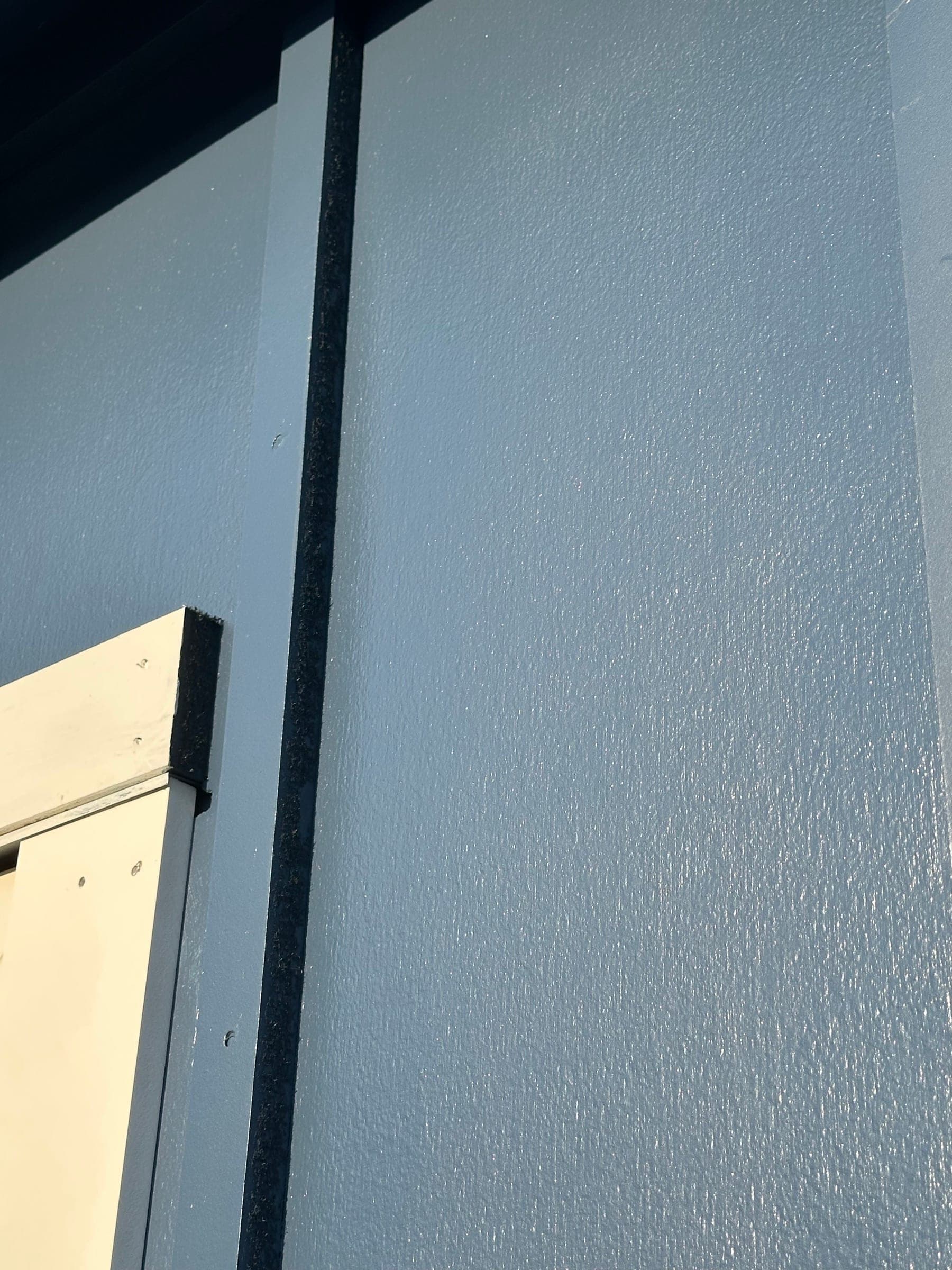 Close detail of the finish on gray-blue siding where a batten meets the field board