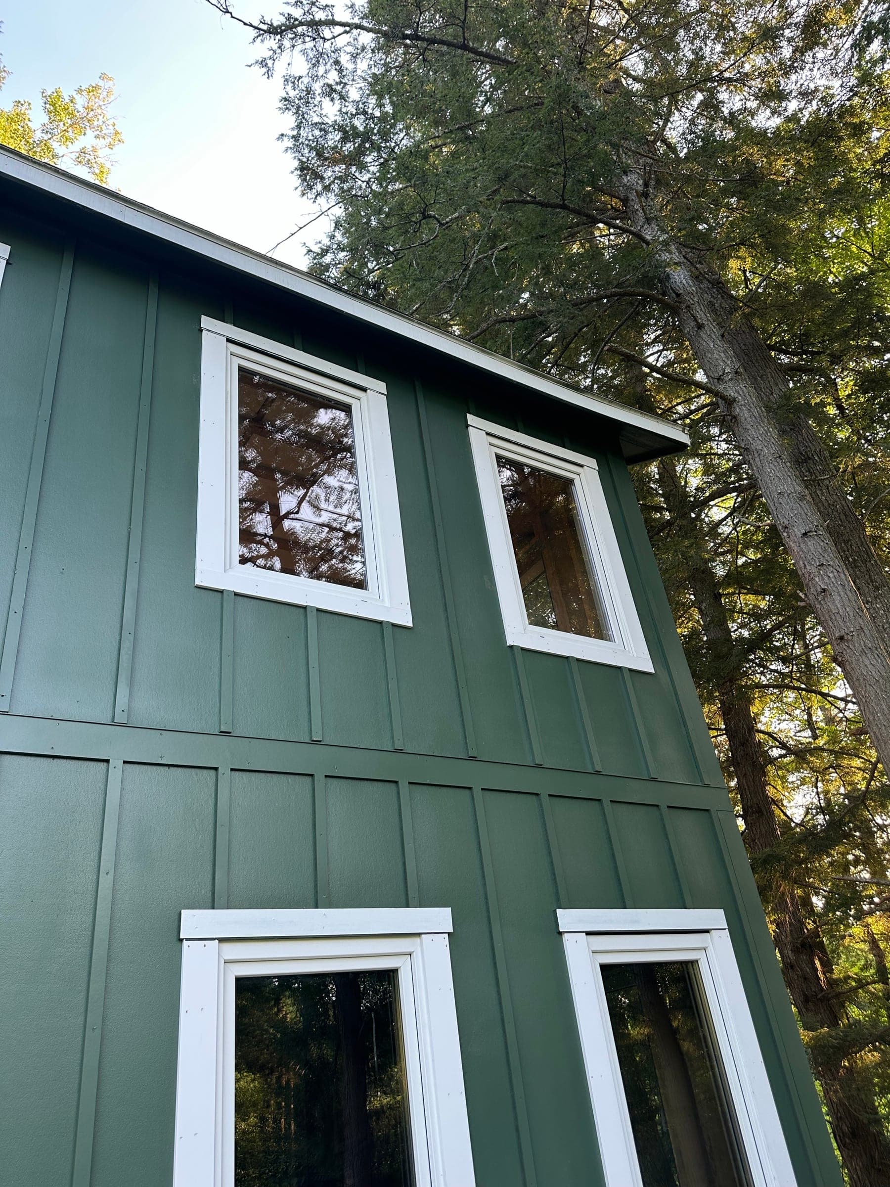 Green board-and-batten siding on a two-story home, looking up past white-trimmed windows