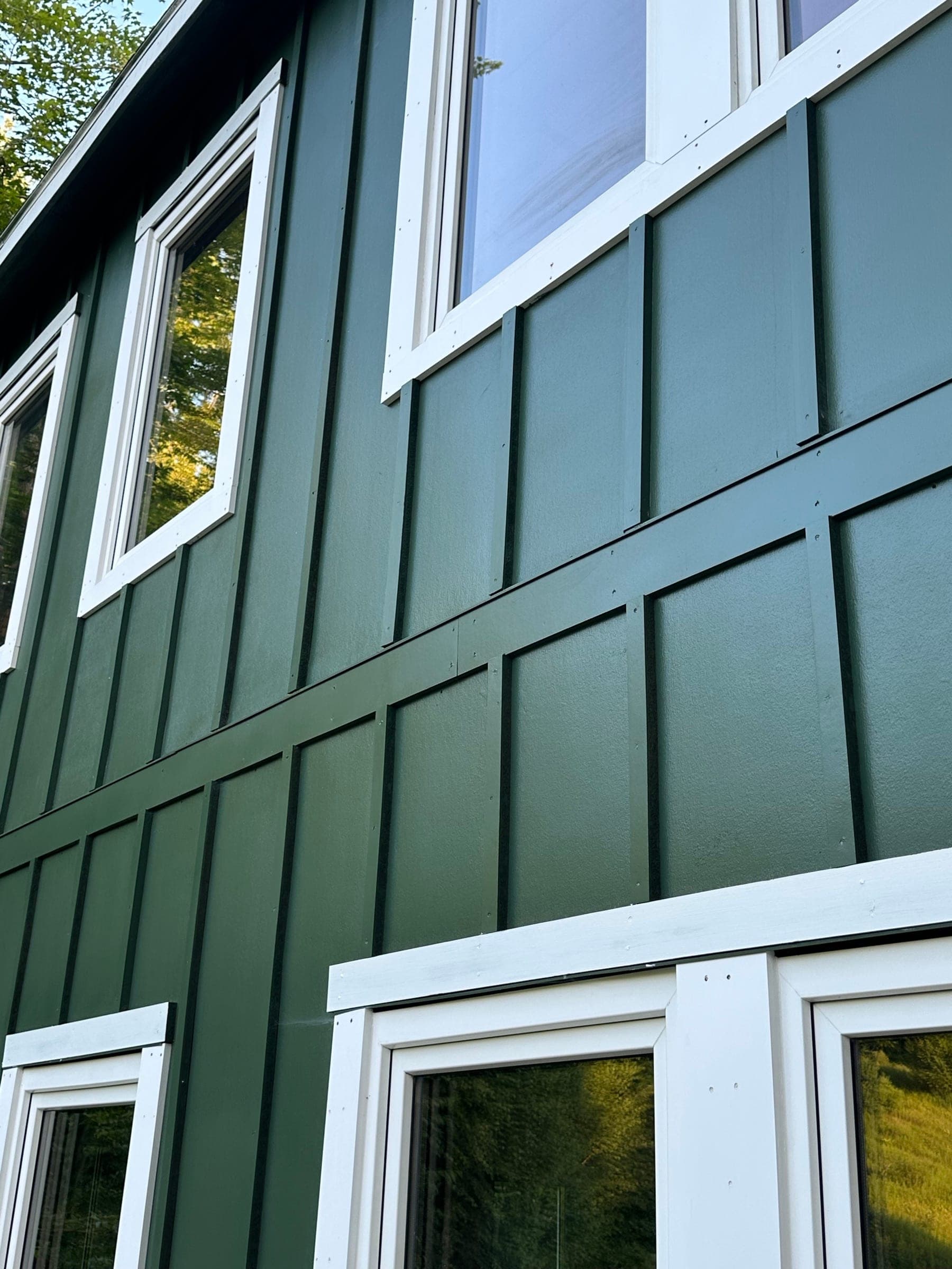 Green board-and-batten siding across a two-story elevation with white window trim