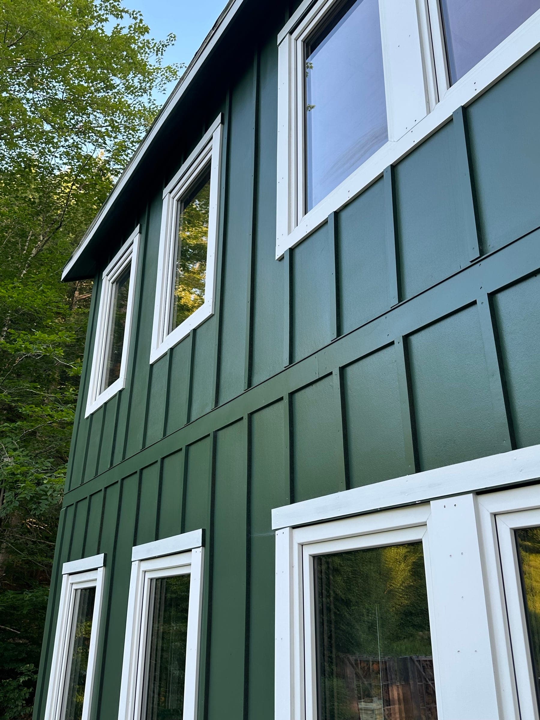 Two-story home in green board-and-batten siding at the edge of the woods