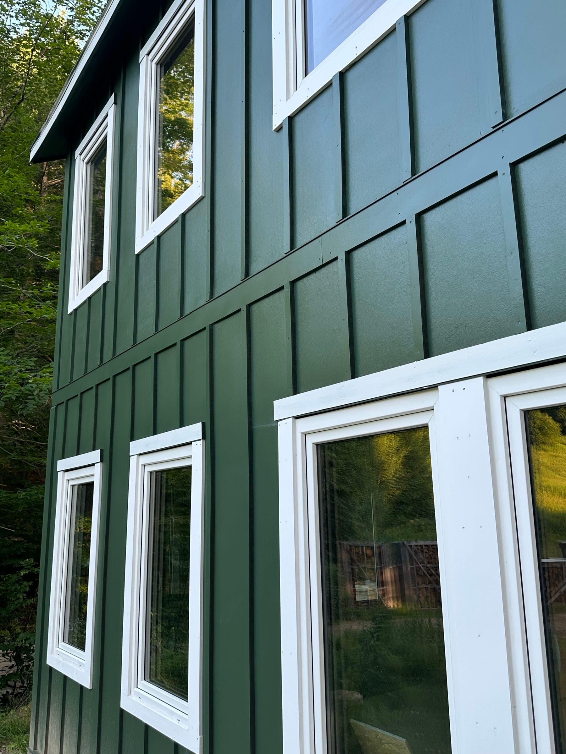 Green board-and-batten siding and white window trim across a two-story elevation